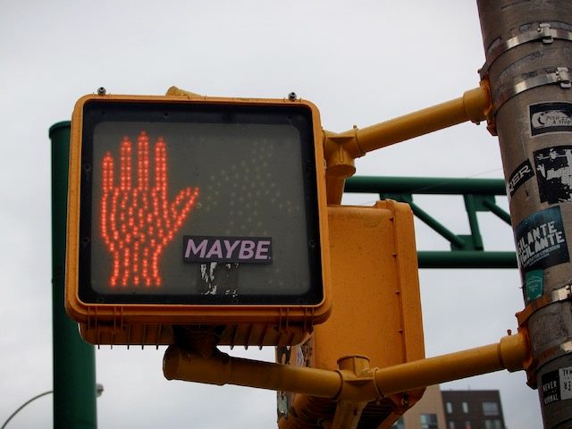 don't walk sign with a sticker saying "maybe" on it