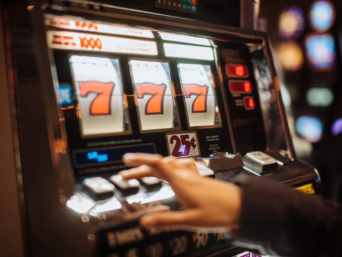 Person's hand playing a slot machine with "7 7 7" showing.