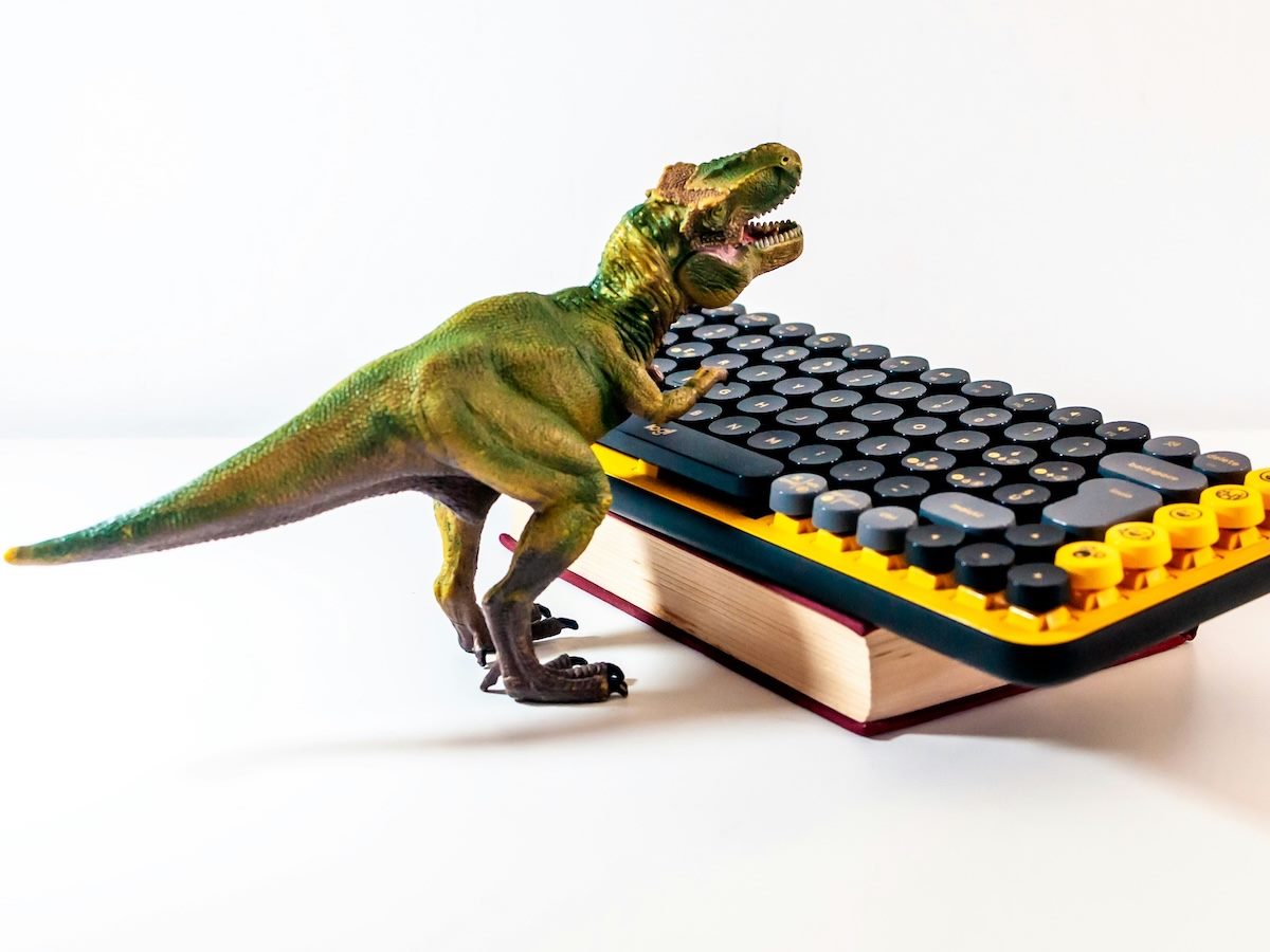 T-Rex toy typing on a mechanical keyboard, propped up on a book