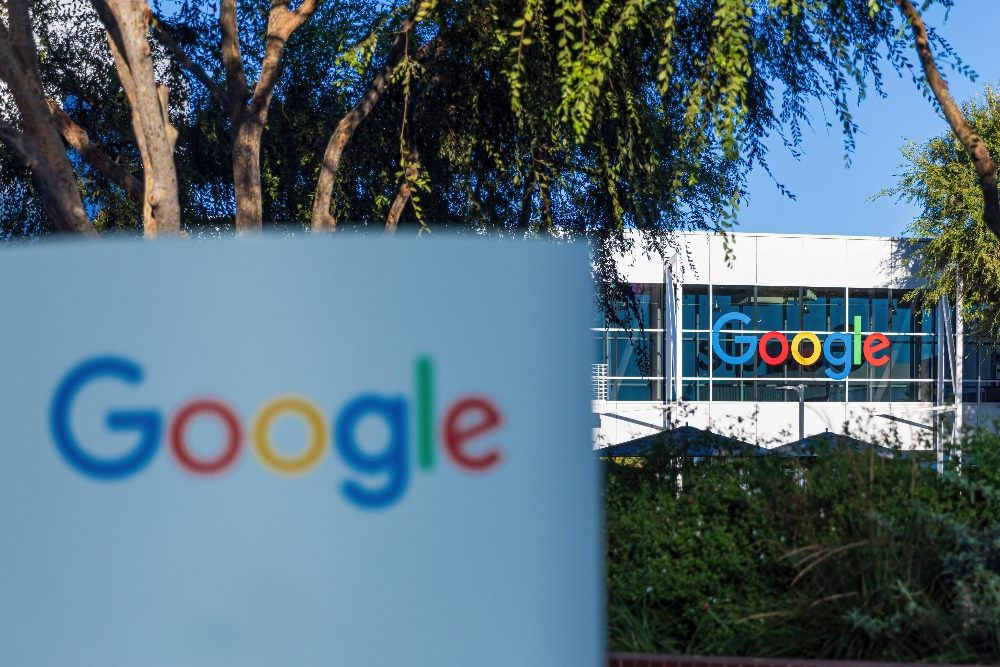 A sign with the Google Name and Logo in Blue, Red, Yellow and Green with headquarters building and trees visible in the background in story about generative AI history.
