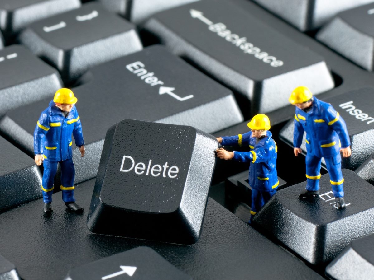 figurines of construction workers removing a delete button from a keyboard 