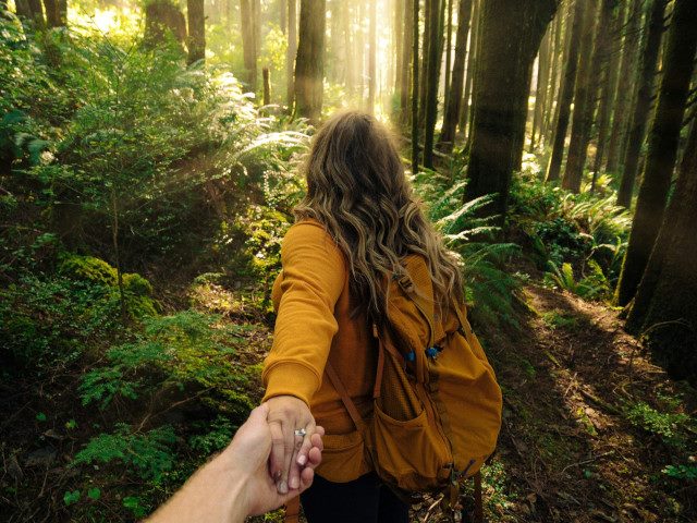 A hiker leads another hiker by the hand on a trail.