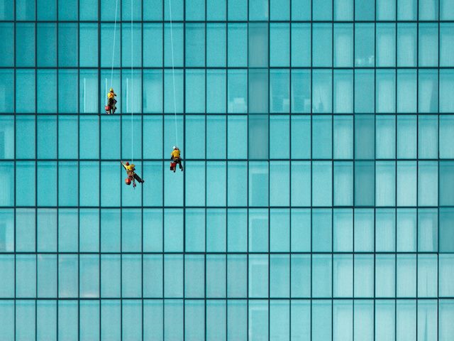 three window washers hanging from ropes, working on  high rise