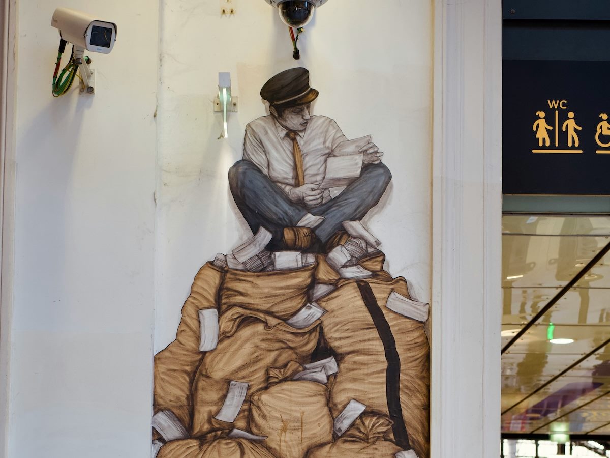 graffiti of a person sitting on top of bags of money, looking at a bill