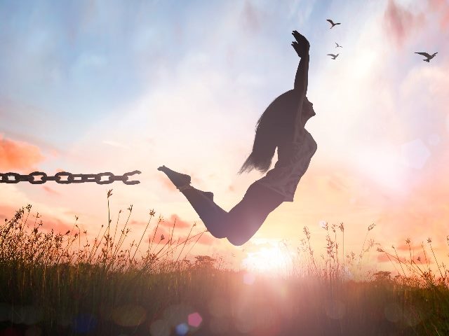 Silhouette of a girl jumping and broken chains at autumn sunset meadow with her hands raised.