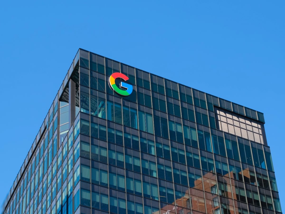 Exterior of a Google office building with the multicolored Google logo on the glass facade against a clear blue sky.