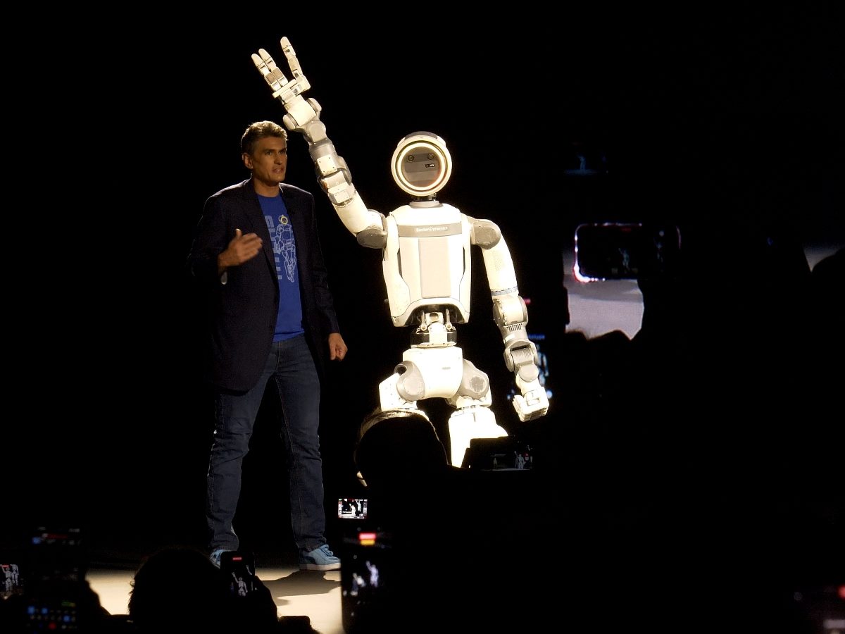 Humanoid robot on stage at CES 2026 raises its arm during a live demonstration, standing beside a presenter under dramatic lighting as attendees record the moment.