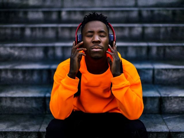 Man sitting down listening to audio on headphones with eyes closed.