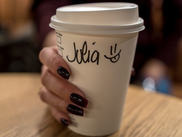 White coffee cup with lid being held in a woman's hand who has red nail polish on and the name Julia with a smiley face is written on the cup.