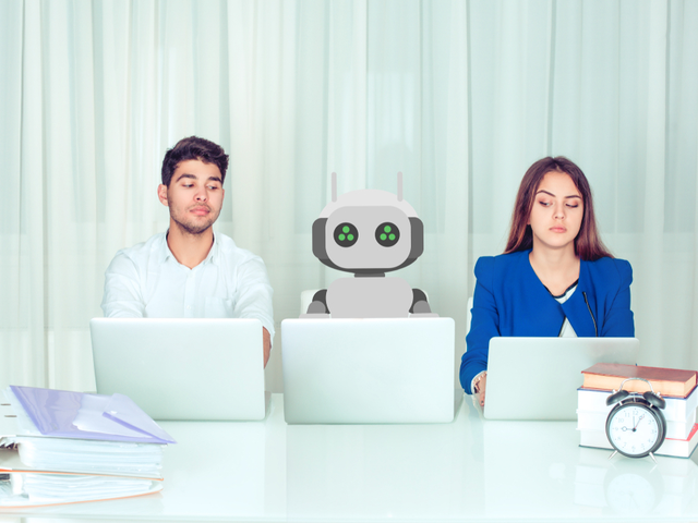 Young man and woman corporate employees with laptops sitting at table with robot colleagu
