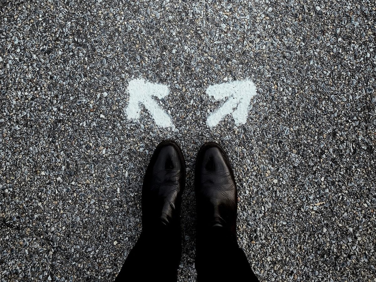 a photograph of the lower part of a person's legs and shoes with two arrows on the ground in front of them. which direction will they choose?