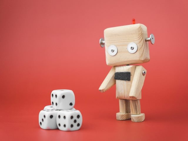 Wooden robot next to the dice on a red background.  