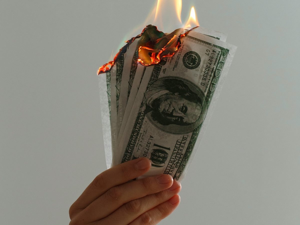 a hand holding a number of $100 bills, all of them on fire