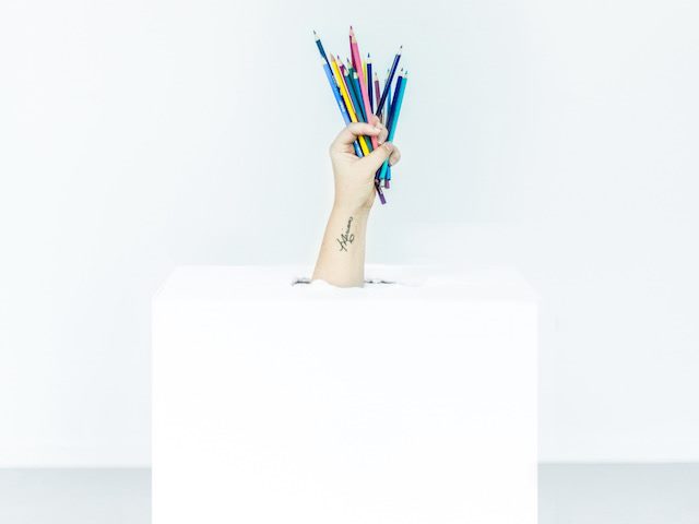 arm holding colored pencils coming out of a white box against a white background