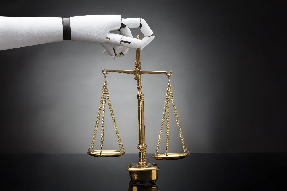 A robot hand holds the scales of justice between its fingertips, suggesting concerns about AI in the workplace, particularly ethics.