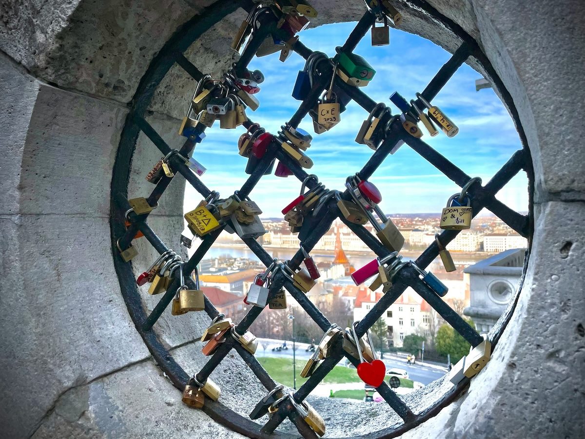 locks attached to a public fence, city visible in the background
