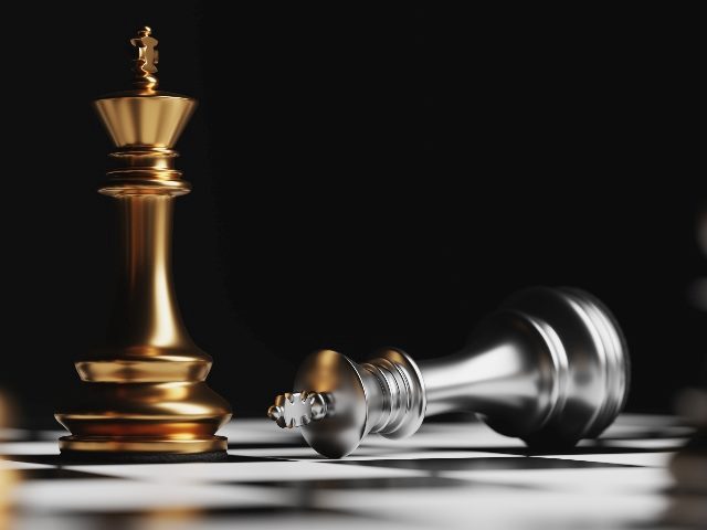 Gold chess piece standing upright, and a silver chess piece lies prone.  