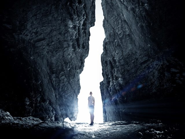 Person standing and looking toward an opening between large rocks.