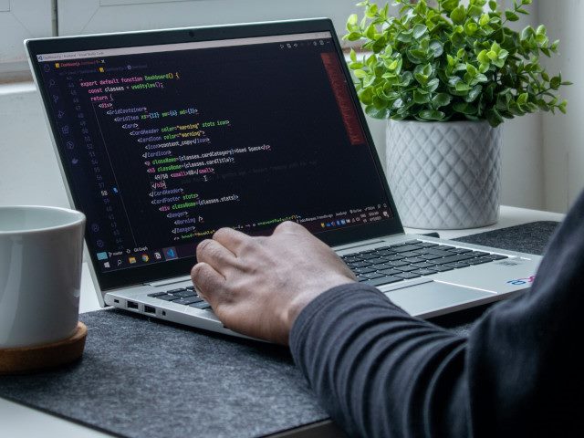 An employee writes code on a laptop computer at a home office.