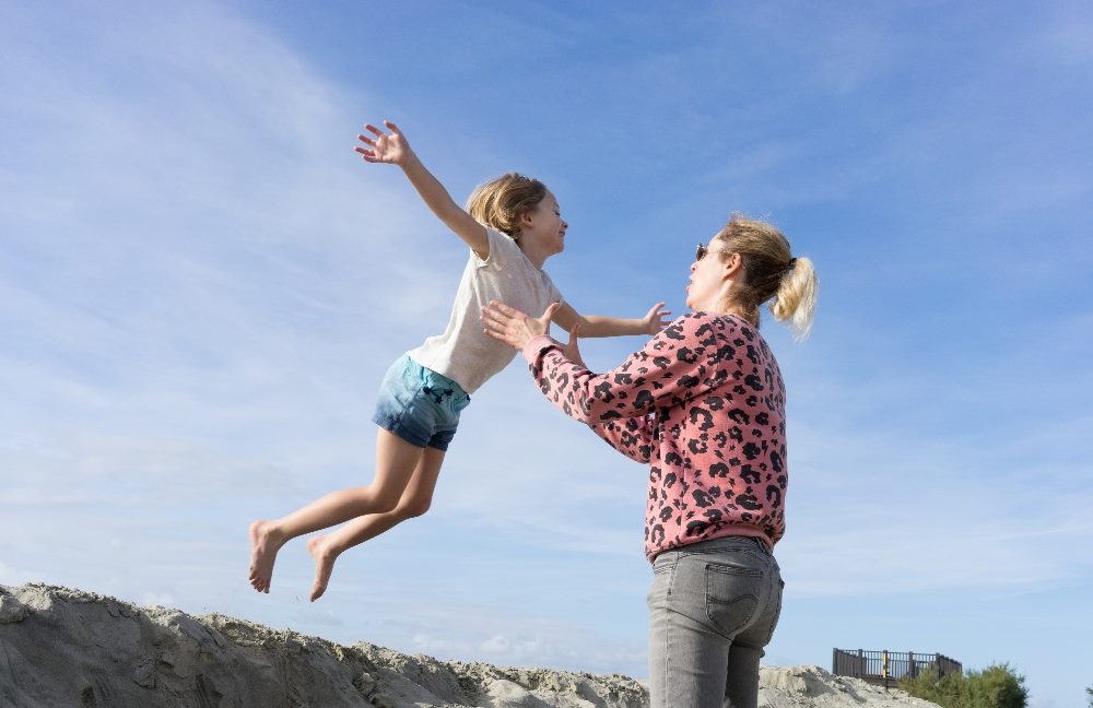 A child wearing shorts and a T-shirt jumps off a sand dune into her mother's waiting arms in piece about Opticon 2023 and building customer retention and brand trust.