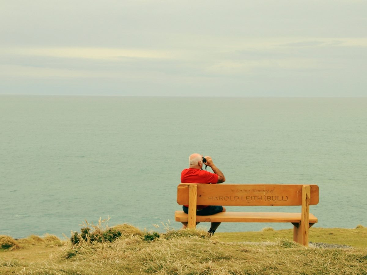A man sitting on a bench with binoculars looking out to the ocean.