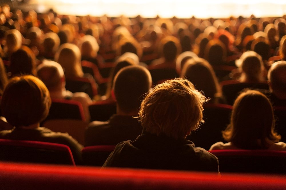 An audience sits in theaters seats in rapt attention to what is happening on the stage in piece suggesting customer experience strategy is akin to theater performances.