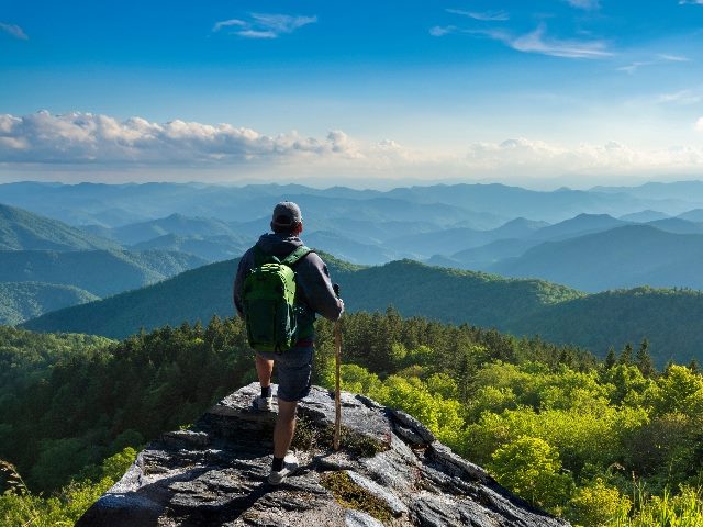 Male hiker standing on top of the mountain enjoying beautiful fall scenery near Asheville, North Carolina, representing the top generative AI use cases -- marketing and customer care.