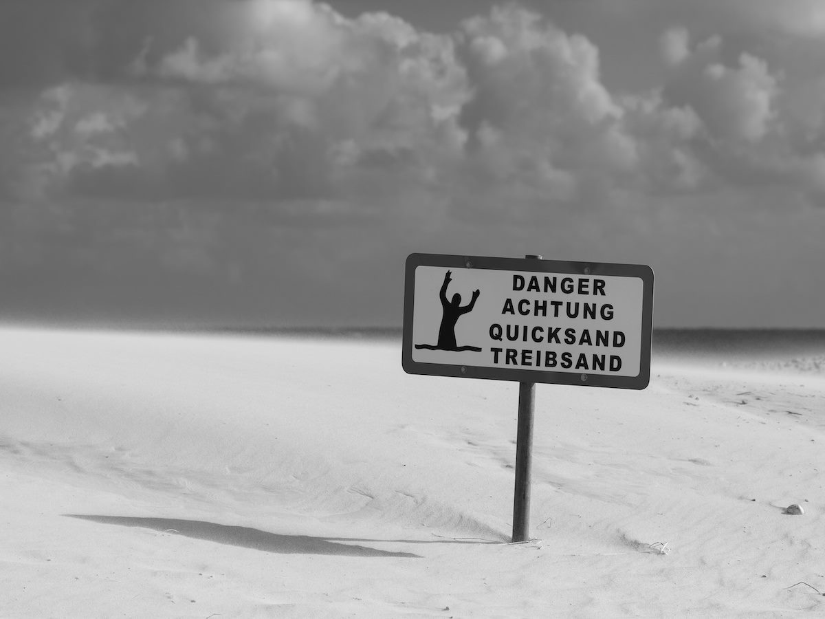 Grayscale shot of the warning sign about quicksand on the beach 