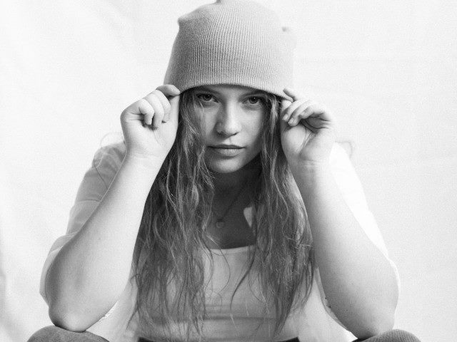 A person sits and holds a beanie on their head.