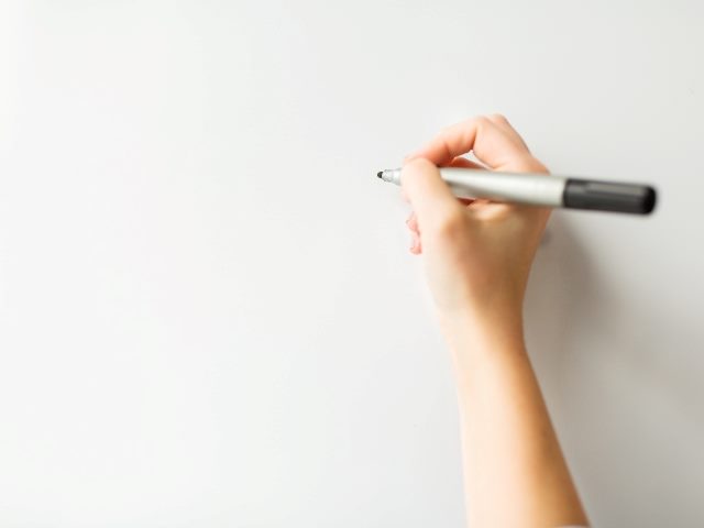 Close up of hand beginning to write something on white board.