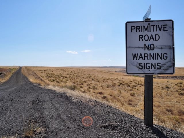 badly paved road with warning sign reading: Primitive Road No Warning Signs