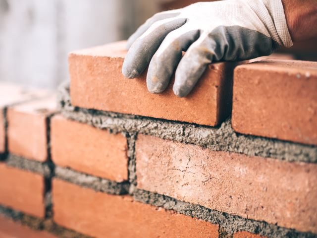 A  close up of industrial bricklayer installing bricks on a construction site - Brick and mortar stores concept