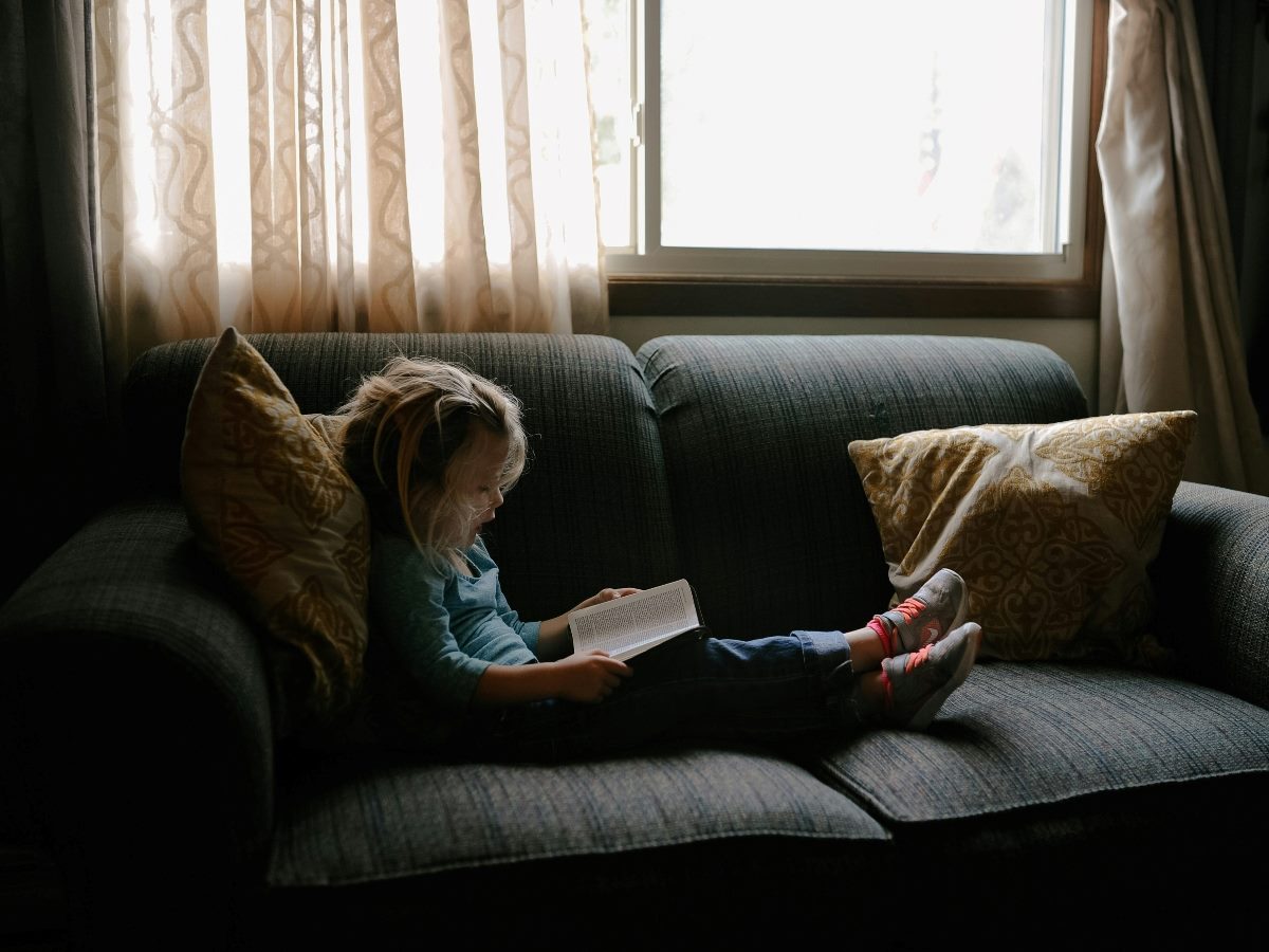 Young girl on a couch reading a book.