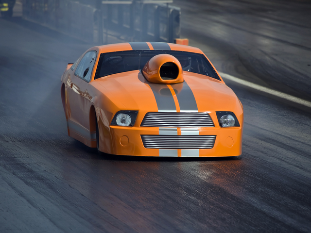 An orange supercharged dragster racing down the track at top speed - DAM concept