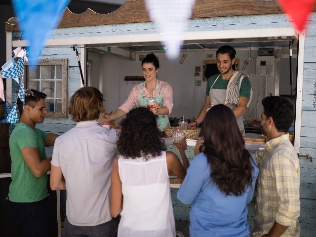 Food truck workers giving juice to customers at counter, signifying a traditional customer interaction that is now being disrupted by AI. 