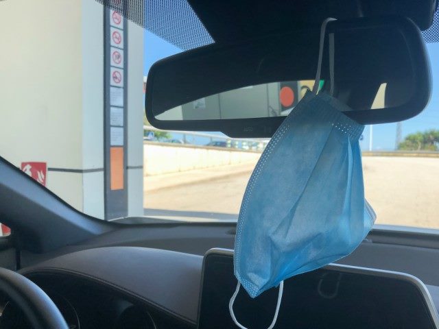 A medical mask hangs over a rear-view mirrors in a car.
