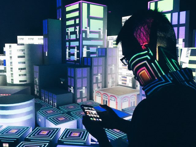 person standing in what looks like an architecture exhibit with strange lights cast on their face as they look at their phone