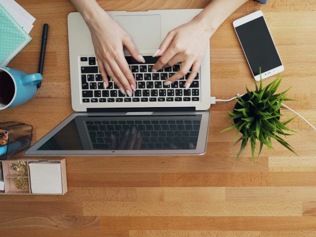 An employee types on a laptop computer on a desk.