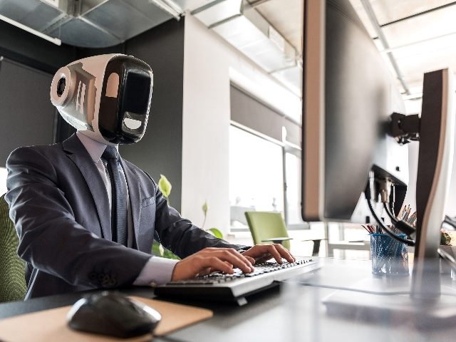 Man with a robot helmet on working on a computer terminal. 