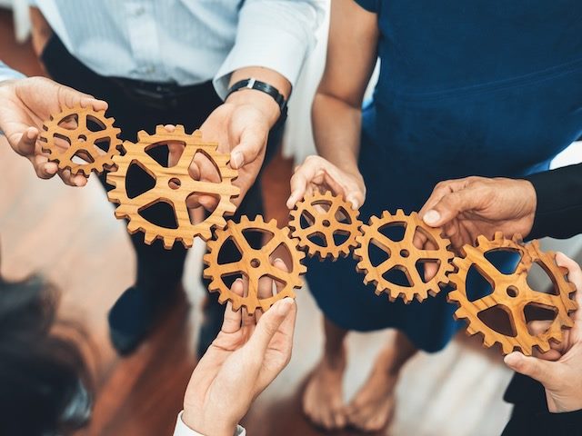 Office workers holding cog wheels together