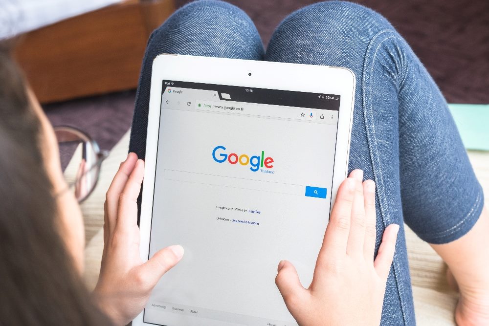 A woman sits on a couch with her feet up using Google Search on her tablet in piece about Google Search changes and artificial intelligence,