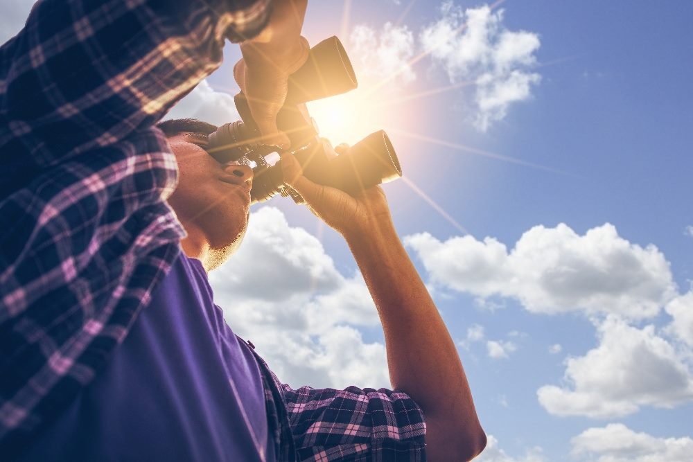 A person wearing a plaid shirt looks through binoculars in piece about customer experience trends for 2024.