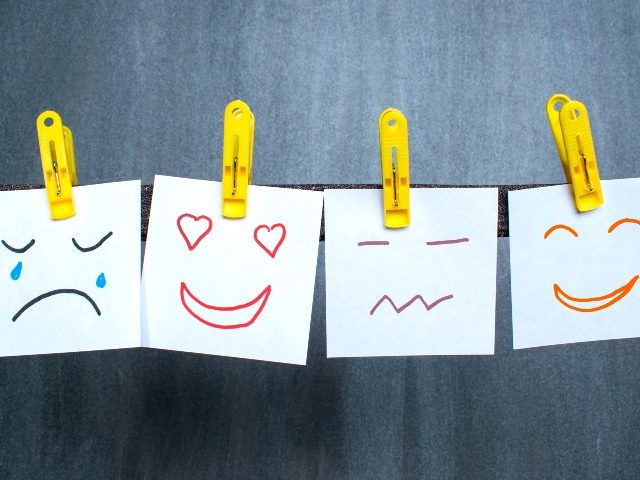 Four pieces of paper hang from a line with clothespins and have faces drawn on them exhibiting feelings, emotions or sentiments. 