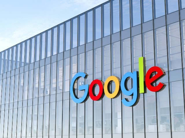Google Signage Logo in Primary Colors, Red, Blue, Green and Yellow, on Top of Modern Glass and Steel Building. with Sky in the Background. 