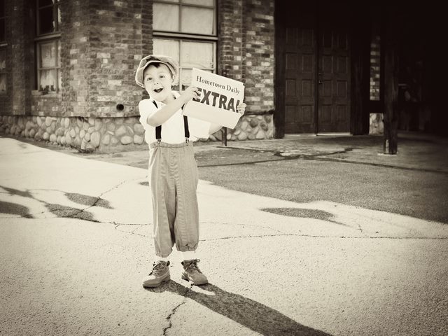 Little old newsboy holding out the newspaper and yelling "Extra".