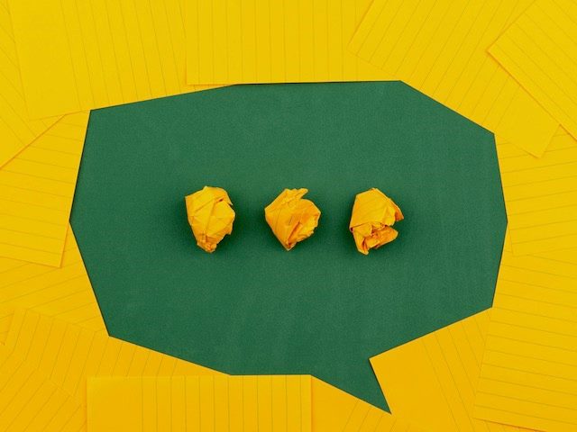 orange sheets of paper lie on a green school board and form a chat bubble with three crumpled papers.