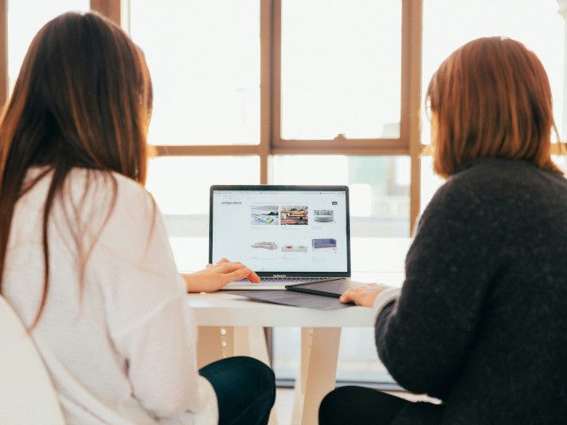Two employees look at a laptop computer screen on a table.