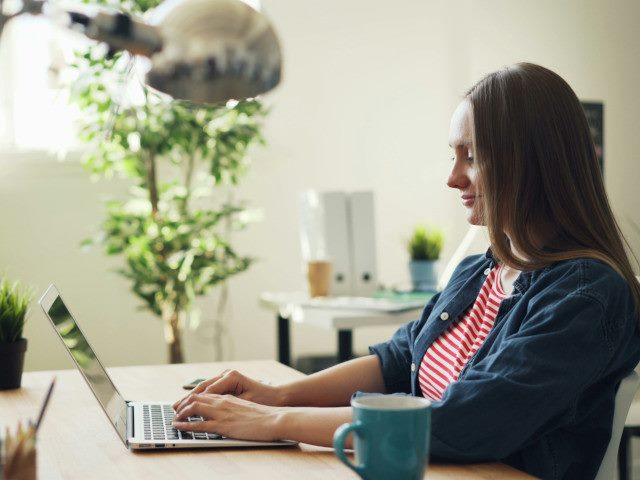 An employee types on a laptop computer on an office desk.