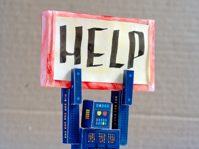 A cardboard robot holding a sign over its head that reads help