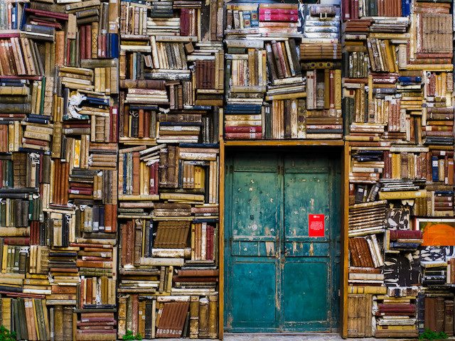 aqua colored door surrounded by haphazard stacks of books